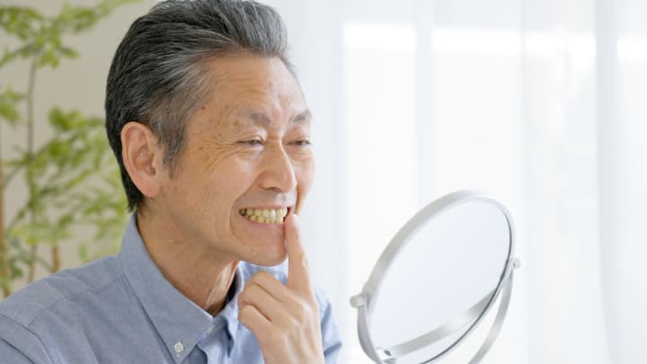 入れ歯が外れるのを気にして鏡を見る男性